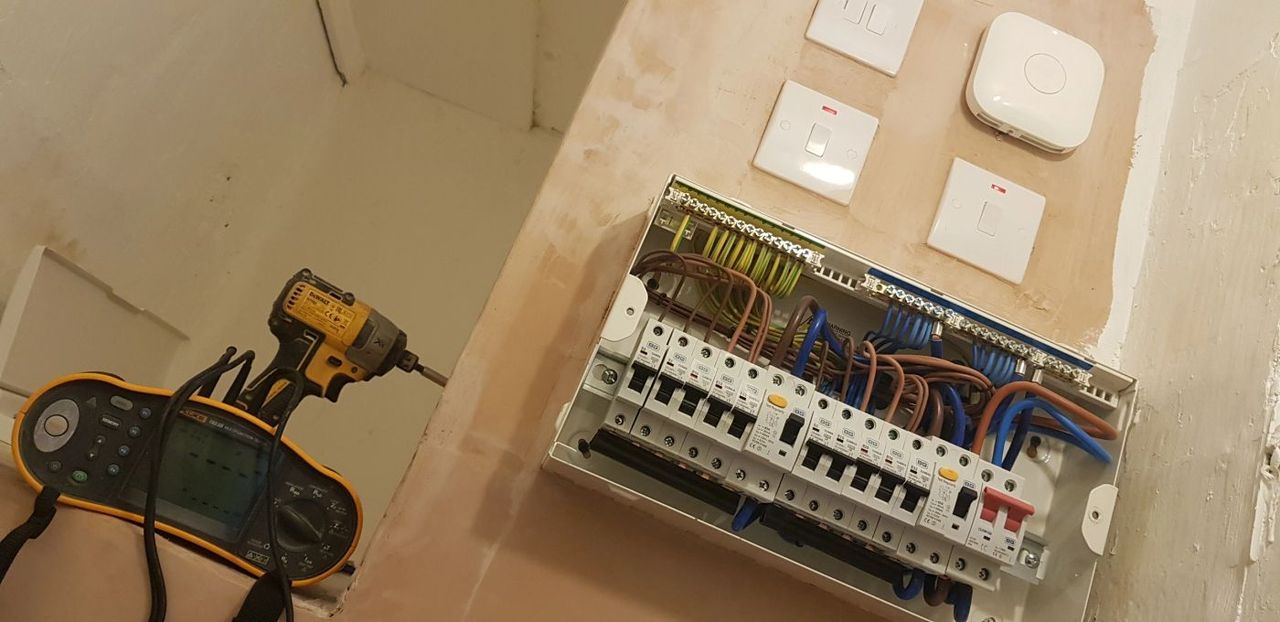 Electrician fitting a consumer unit, impact driver in hand